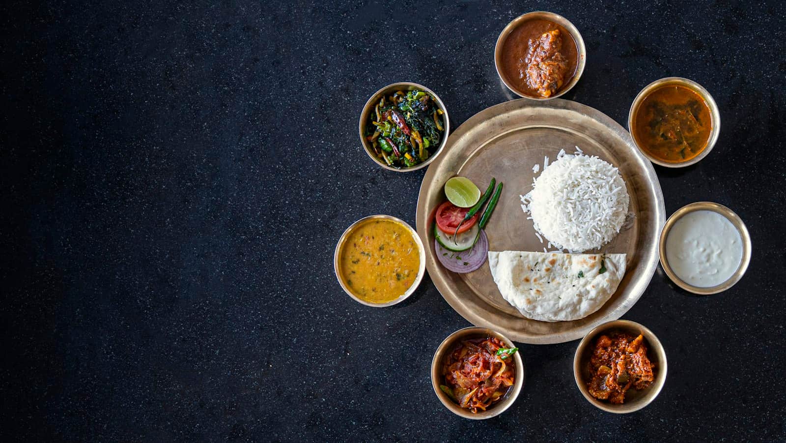 Overhead thali of small bowls on a dark table