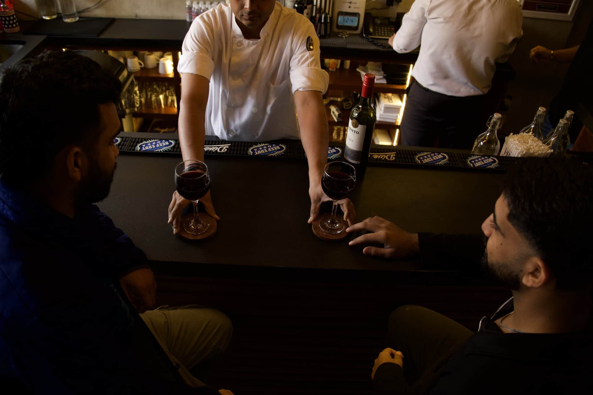 Two glasses of red wine set down on the bar at Angel for two guests, a bottle and the back bar behind