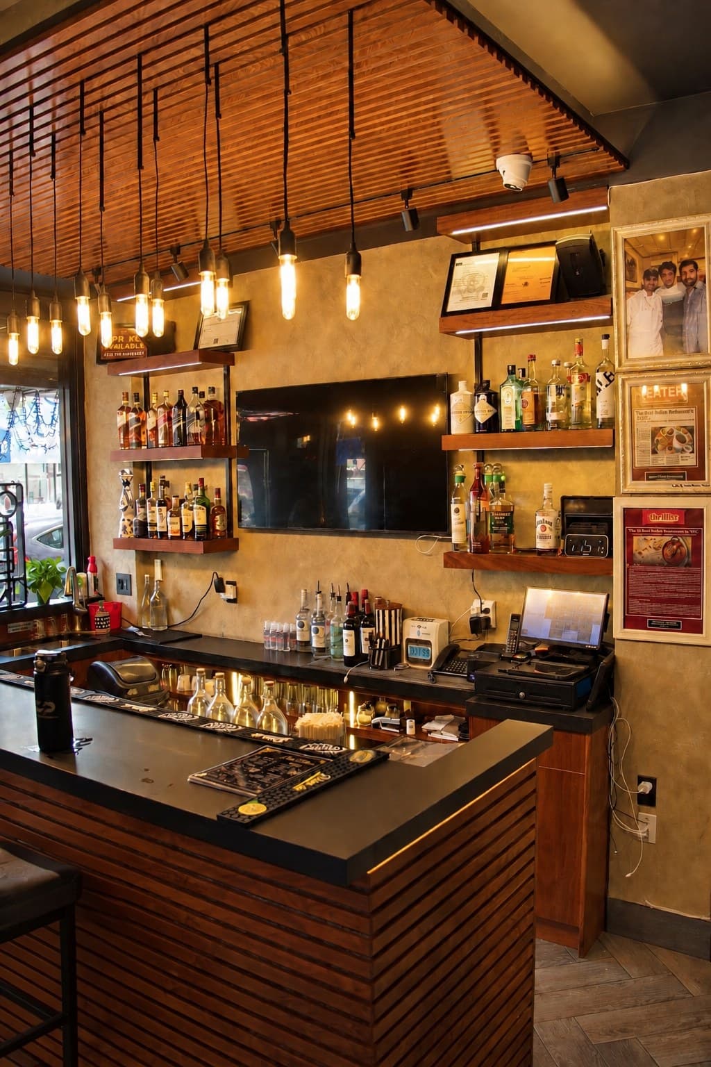 The bar at Angel: Edison bulbs hanging from a wooden slat ceiling, shelves of bottles, framed press features on the wall and a slatted wood counter