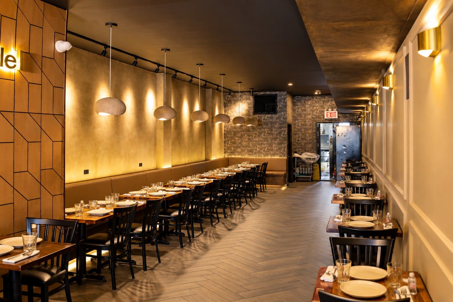 Angel's dining room set for service: stone pendant lamps over a long banquette, laid tables and a herringbone floor